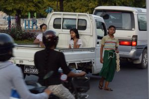 赤信号待ちの車に新聞や交通安全の御守りの花を売る少年